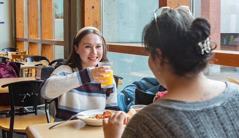 Two SPU students sit at a table next to the window while enjoying their meal in Gwinn Commons